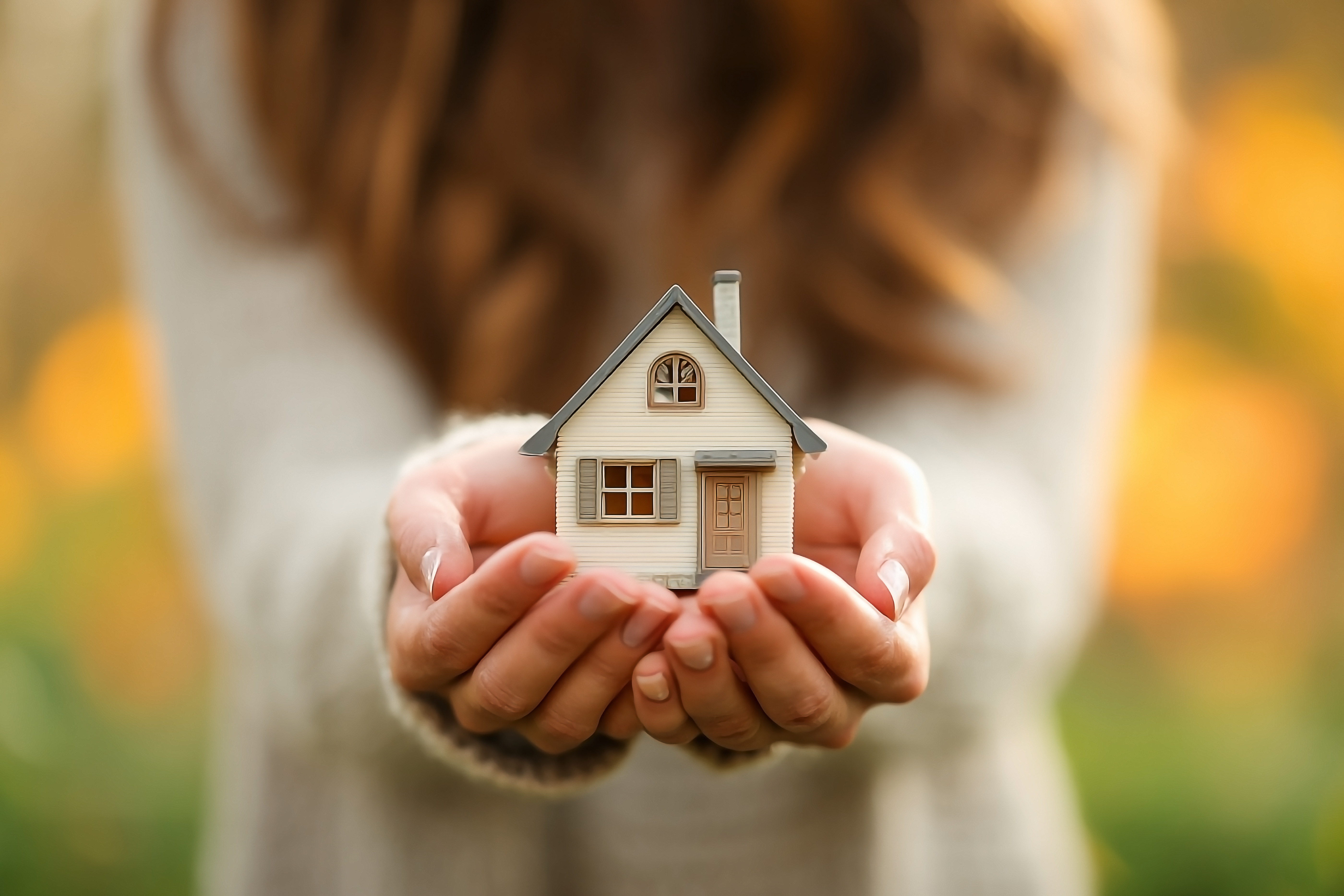 Hands gently holding a small wooden house with a heart cutout